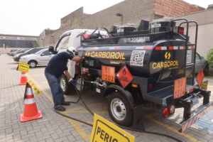 Caminhão da Carboroil realizando abastecimento emergencial de diesel em estacionamento, com sinalização de segurança e identificação de material inflamável.