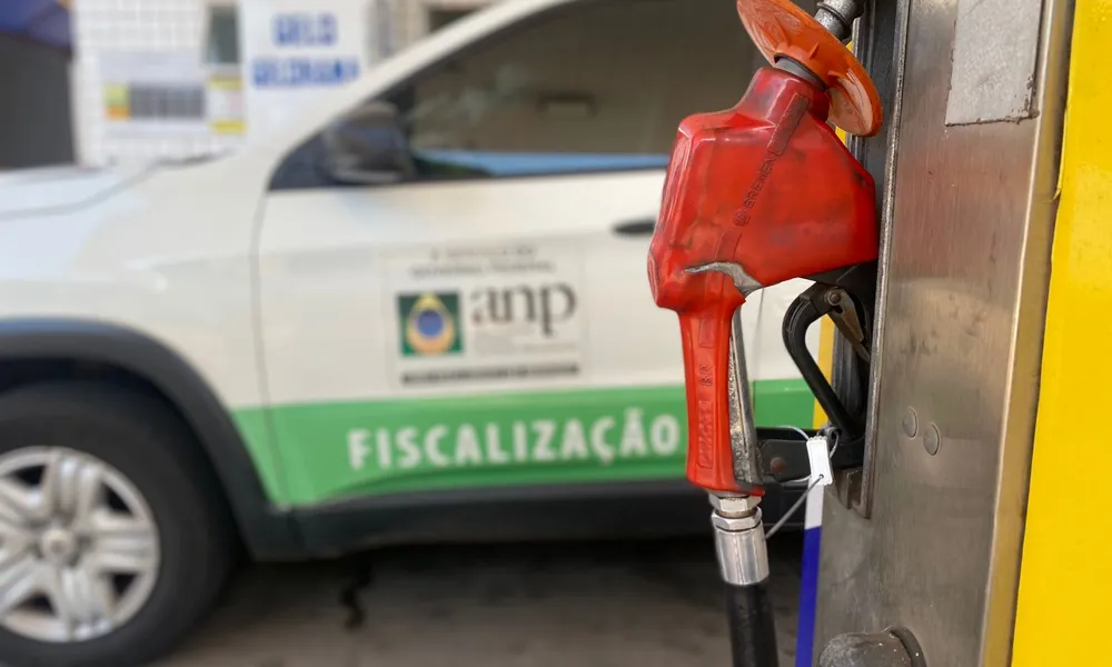 Bomba de combustível lacrada em posto com veículo de fiscalização da ANP ao fundo.